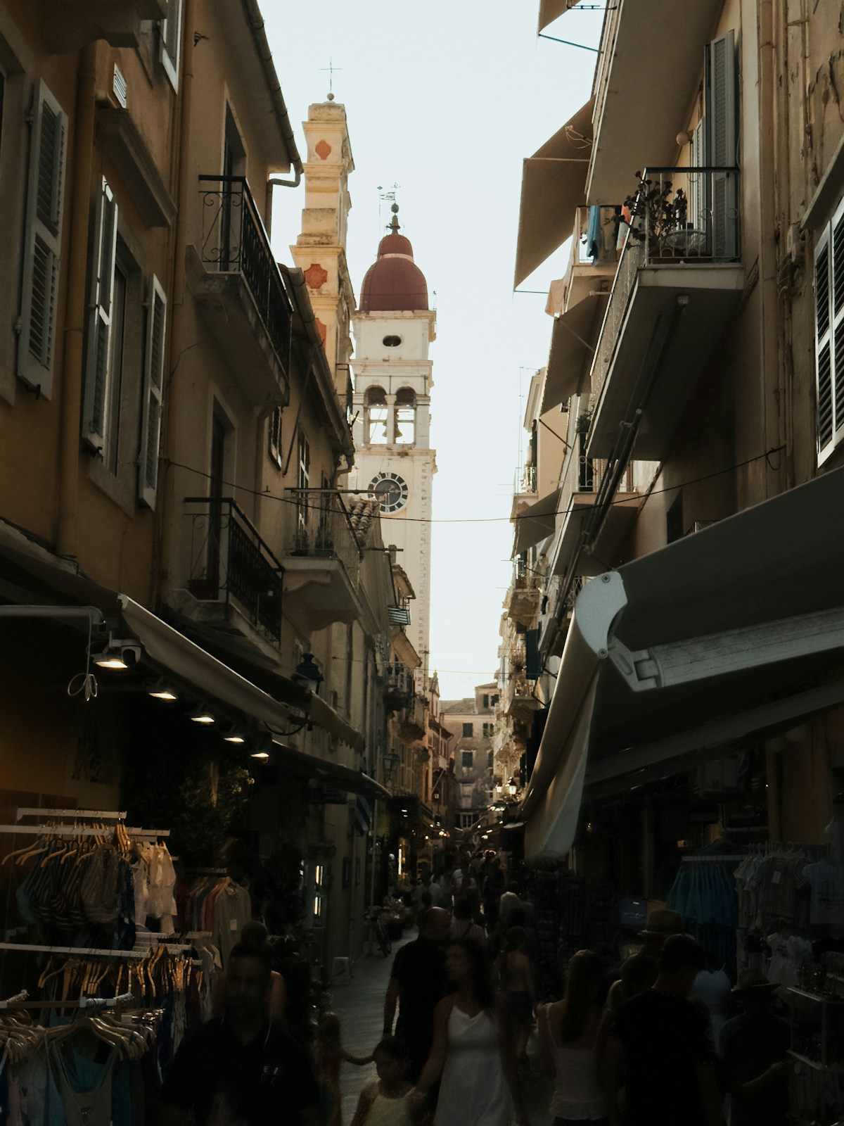 Busy shopping street leading to a bell tower in Corfu Old Town, Greece