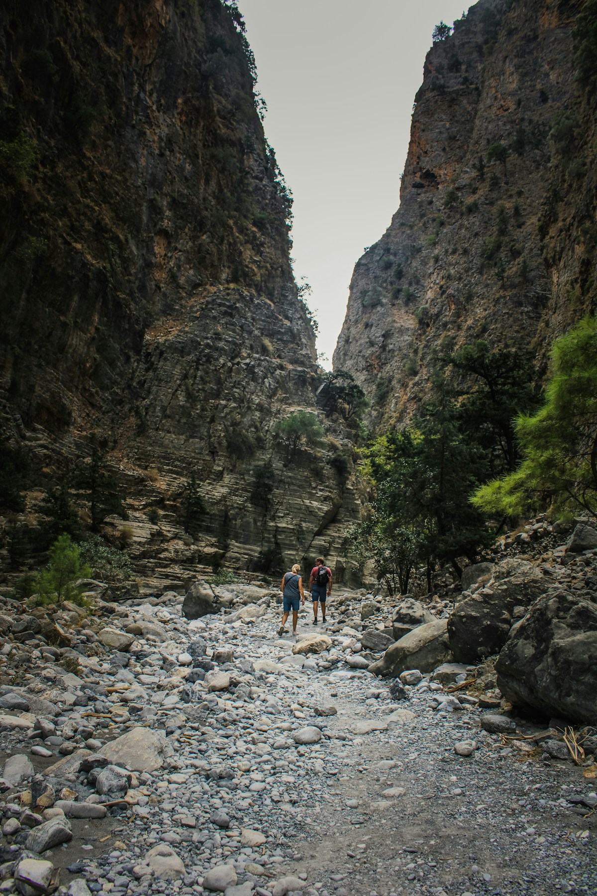 Two hikers walking through the rocky floor of a narrow gorge in Greece