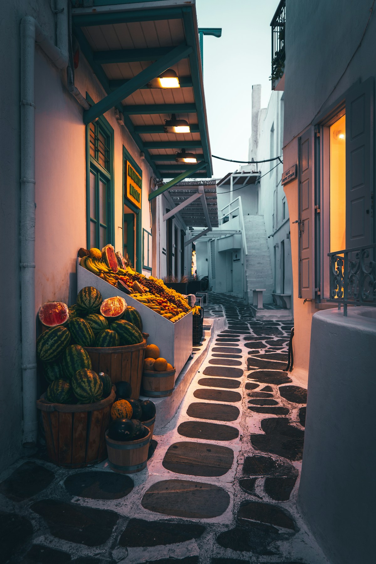 Cobblestone alley with a fruit and vegetable stall at dusk, Mykonos Town, Greece