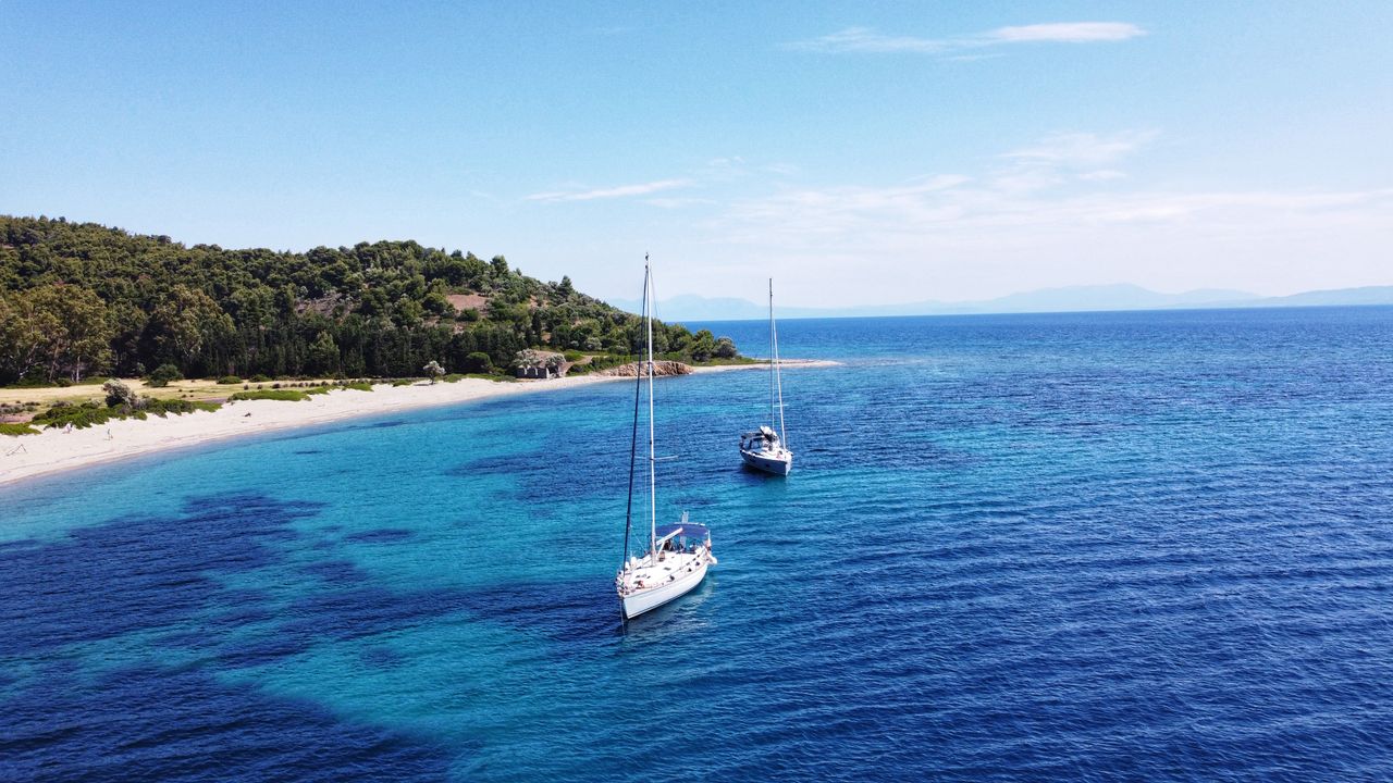 Sailing yachts anchored in a turquoise bay off a sandy beach on Skiathos, Greece
