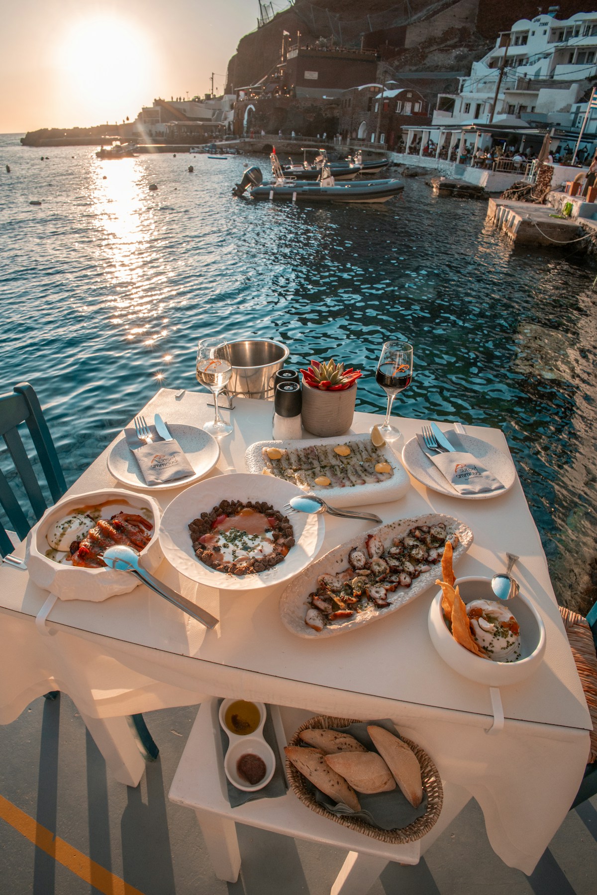 Table of Greek dishes and wine by the waterfront at sunset in Fira, Santorini, Greece