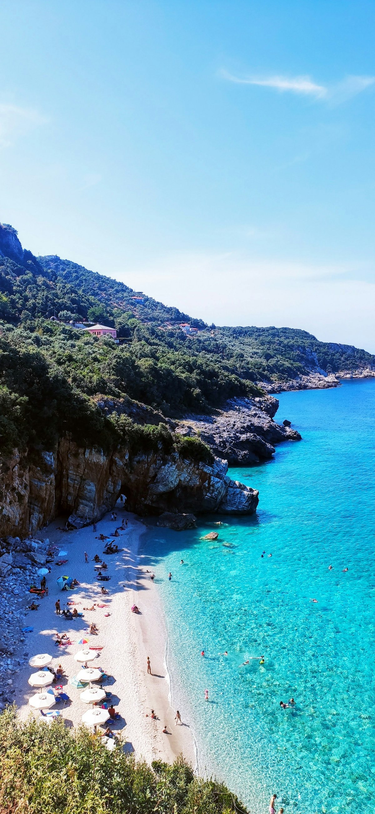 Turquoise Aegean water at a Greek beach with white pebbles and forested hills behind