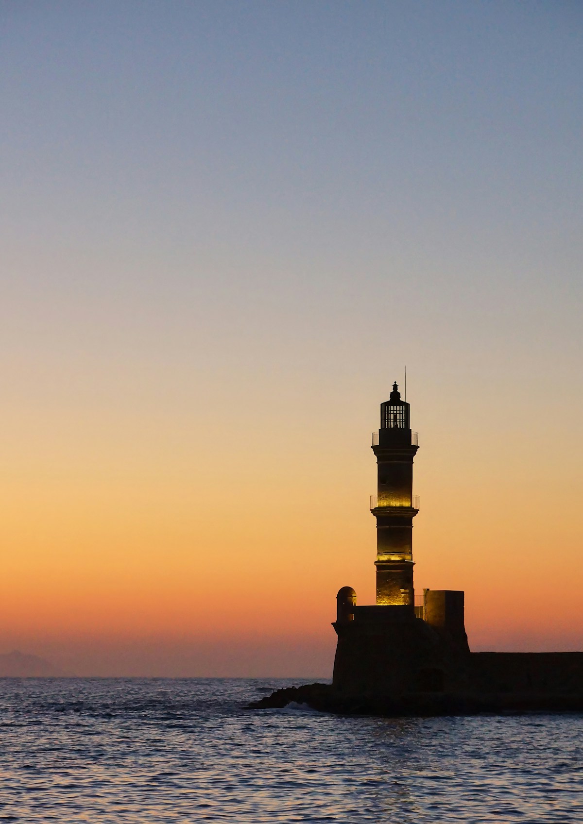The Chania lighthouse silhouetted against a golden sunset sky at the entrance to the Venetian harbour, Crete