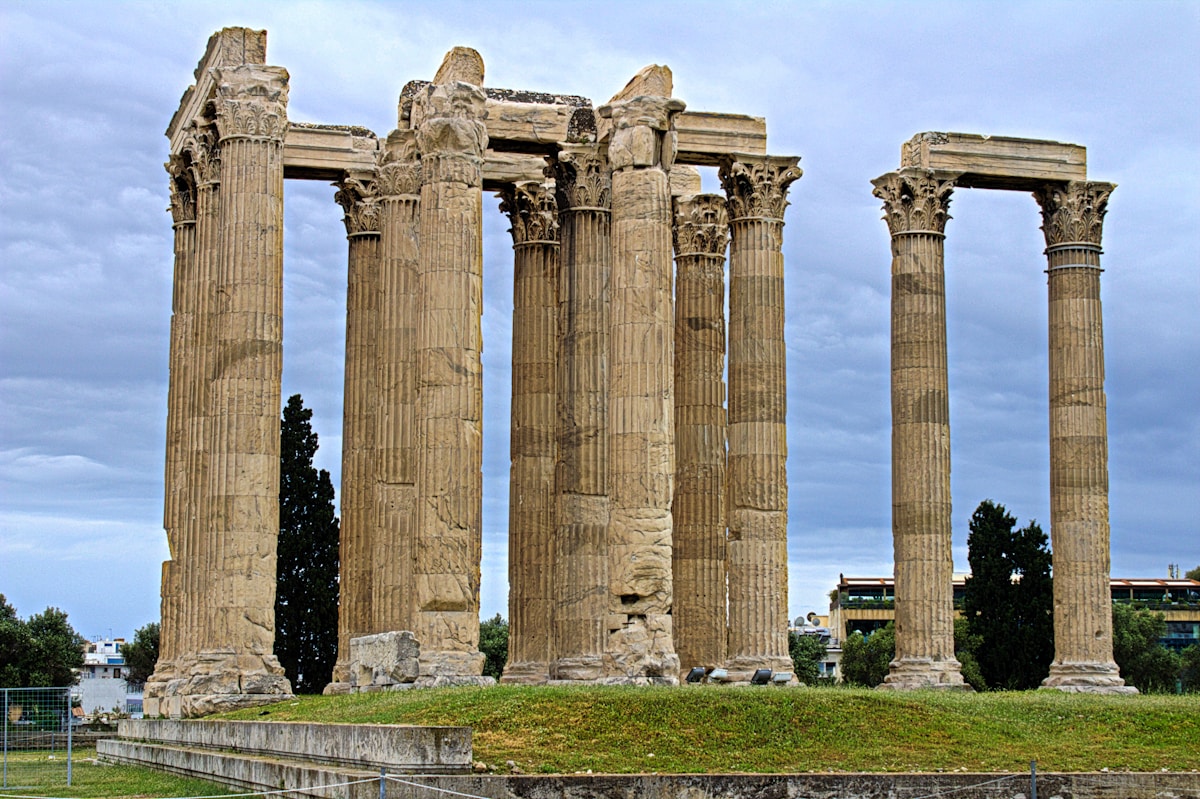 The fallen columns of the Temple of Zeus at Ancient Olympia with pine trees in the background
