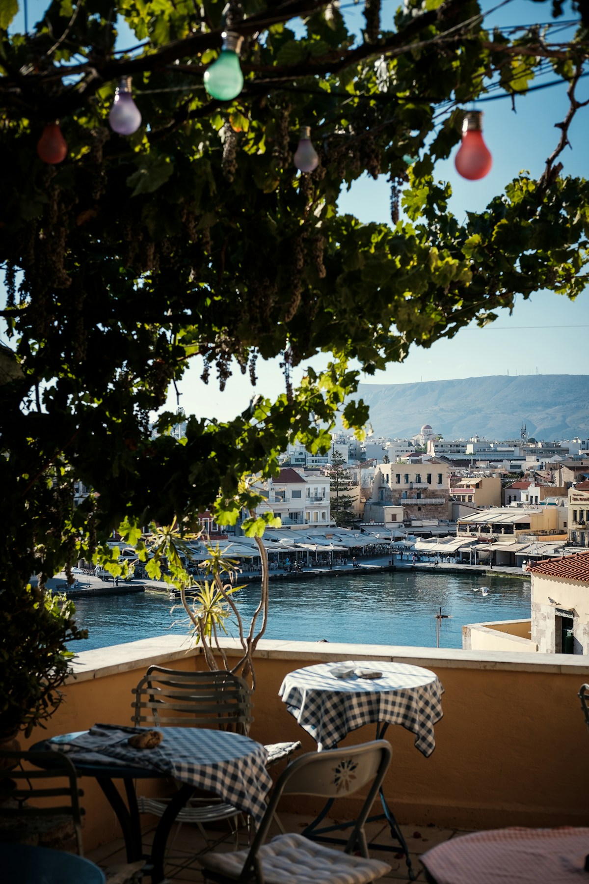 Rooftop restaurant terrace with checked tablecloths and a view of Chania harbour and lighthouse, Crete, Greece