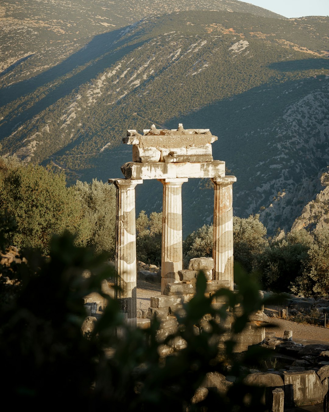 The Tholos of the Sanctuary of Athena Pronaia at Delphi — three ancient Doric columns with mountains and olive groves behind