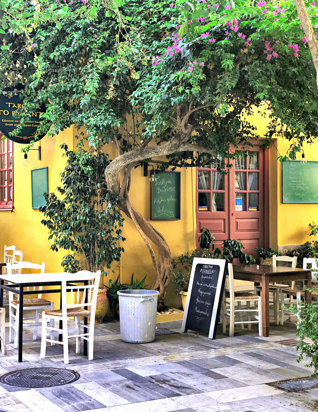 A colourful yellow taverna exterior with tables set outside under a large tree in the old town of Nafplio, Greece