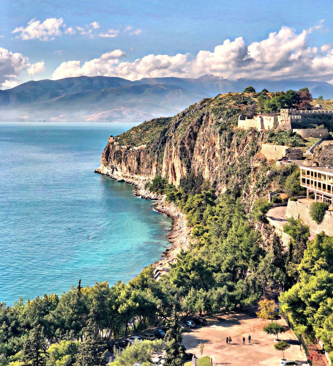 The rocky coastline below the Palamidi fortress in Nafplio, with turquoise Argolic Gulf water and mountains in the background