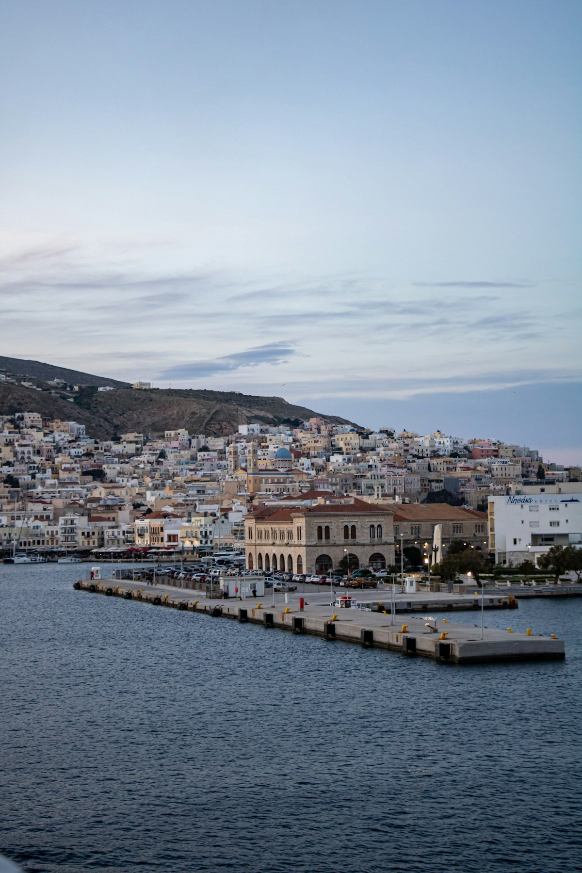 Coastal Greek town with neoclassical buildings, pier, and hillside at dusk