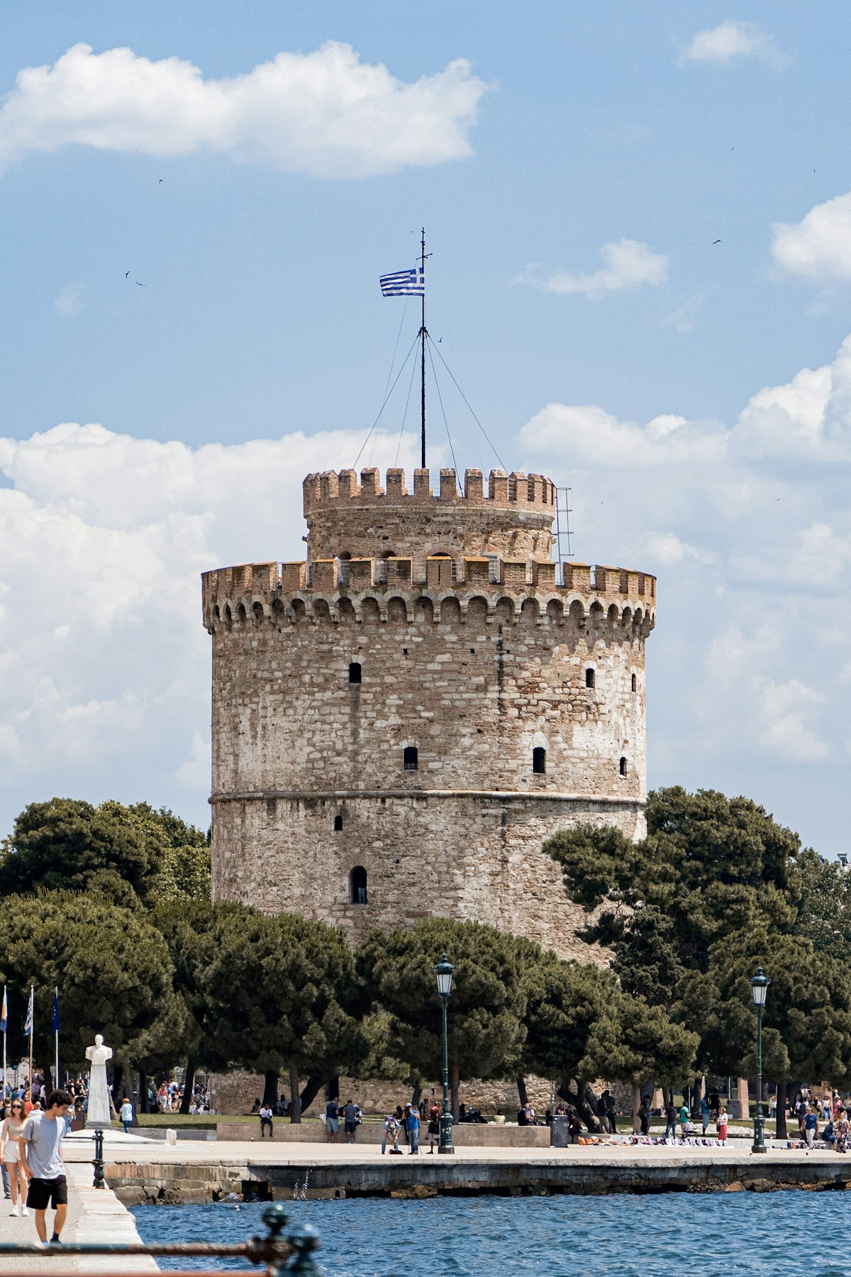 The White Tower of Thessaloniki rising above the waterfront on the Thermaic Gulf, Greek flag flying at the top