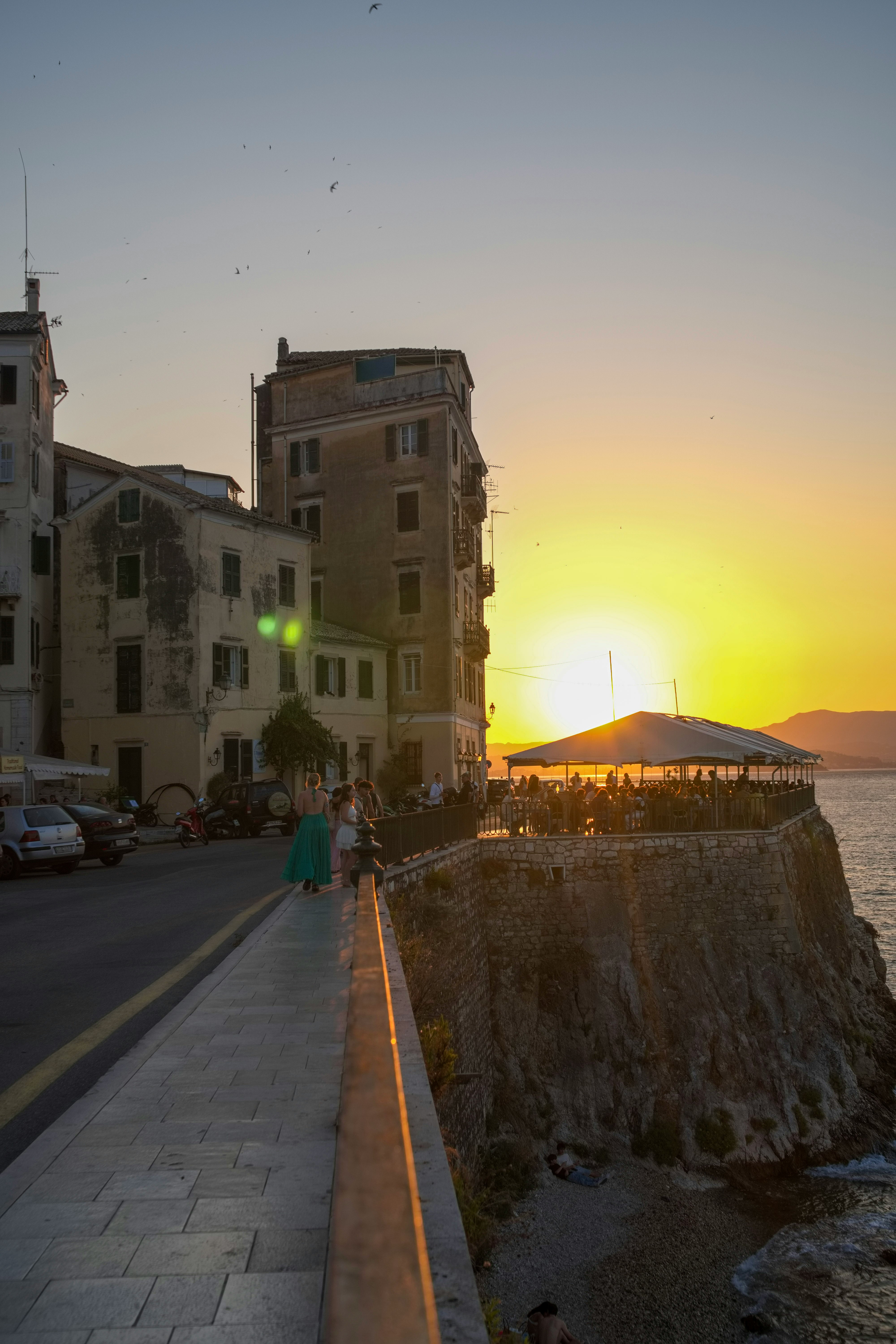 Sunset over Corfu Old Town with a cliffside restaurant terrace overlooking the sea
