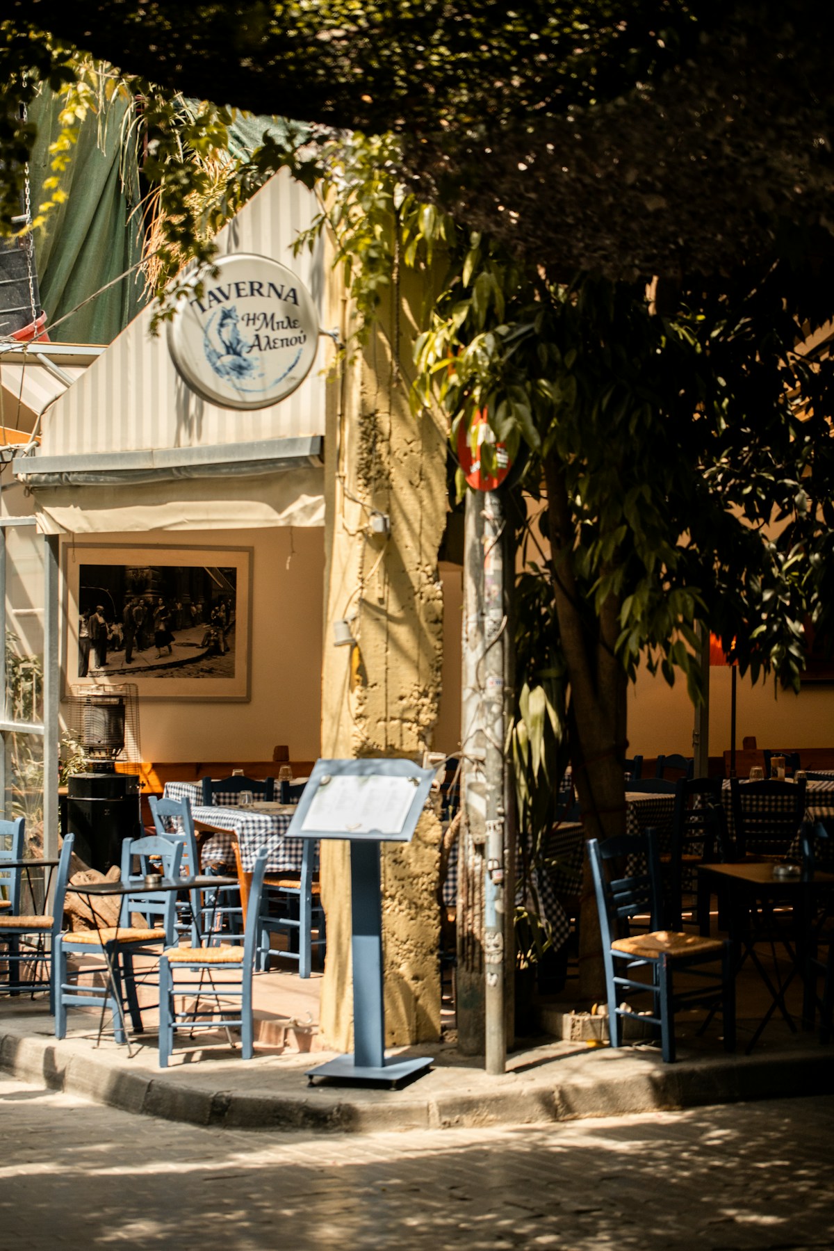 Traditional Greek taverna exterior with blue chairs and TAVERNA sign in Athens