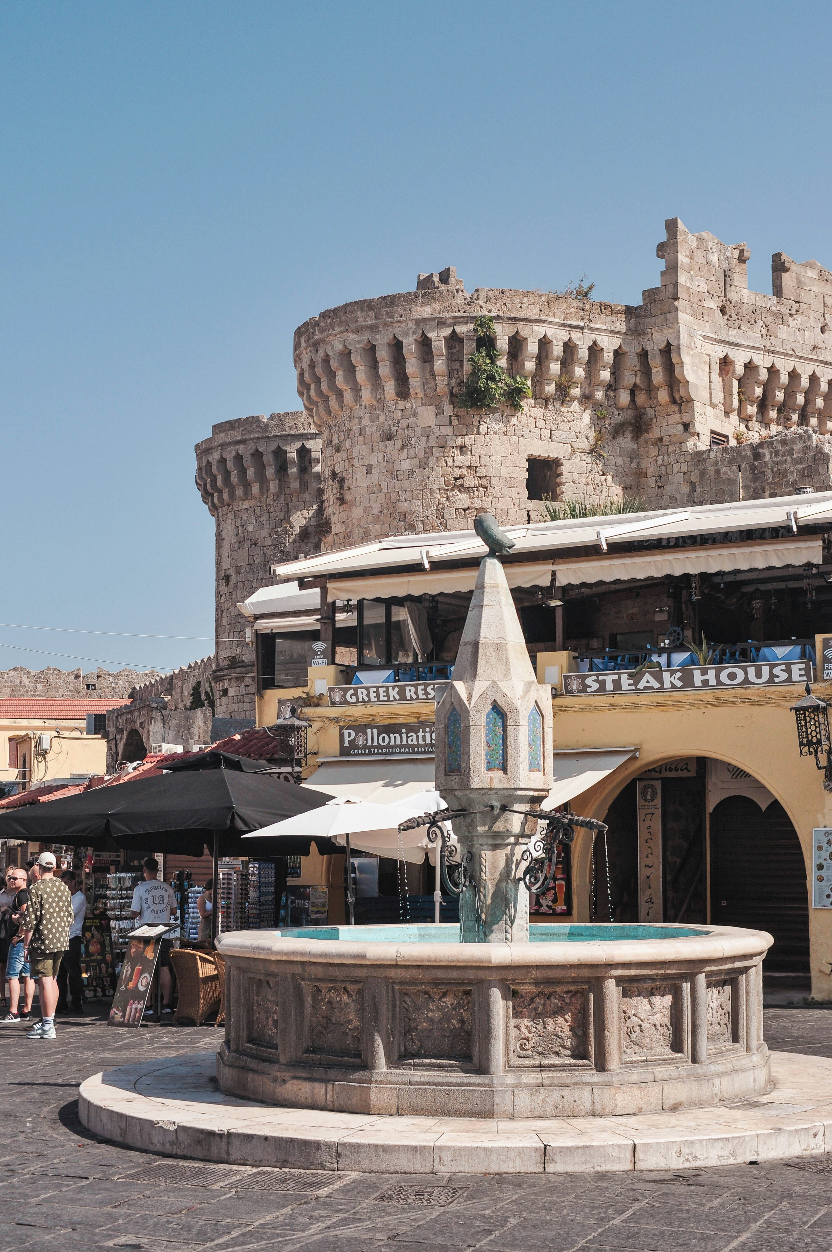 Hippocrates Fountain in Rhodes Old Town with the Grand Master's Palace and restaurant signage visible