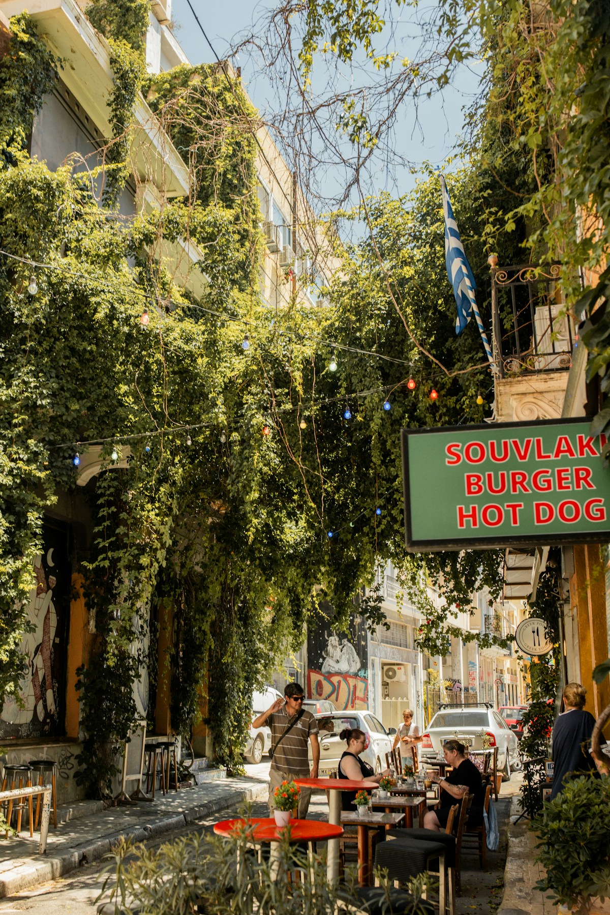 Athens street food scene with souvlaki sign and outdoor dining on vine-covered street