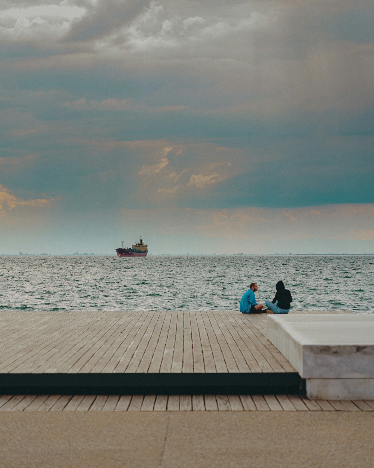 Couple sitting on a waterfront dock under a dramatic stormy sky, Thessaloniki, Greece