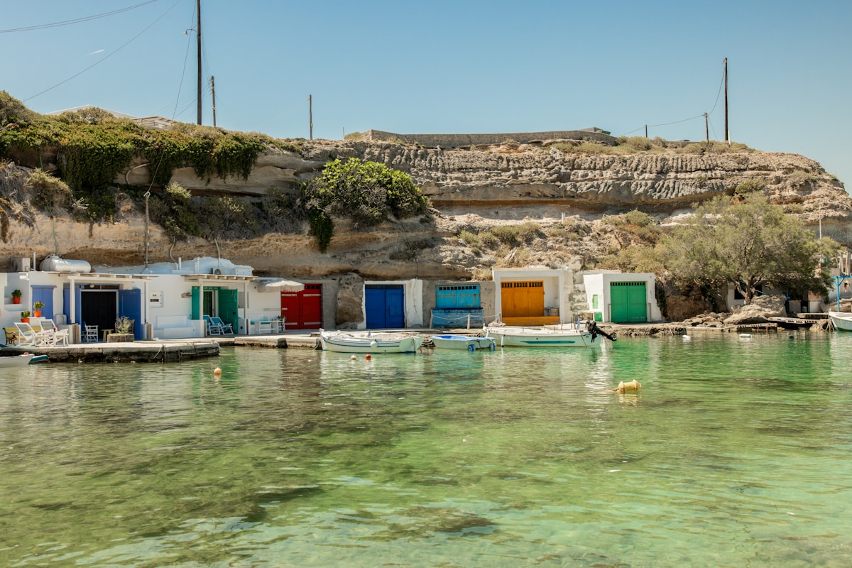 Colourful fishing boathouses built into volcanic rock above crystal clear water, Milos, Greece