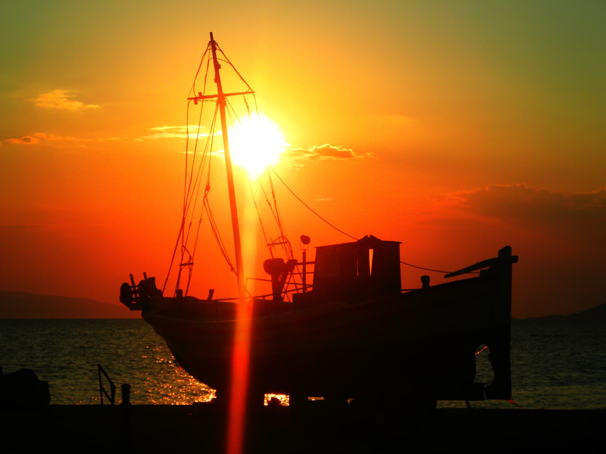 Traditional fishing boat silhouetted at sunset in Aegina harbour, Saronic Gulf, Greece