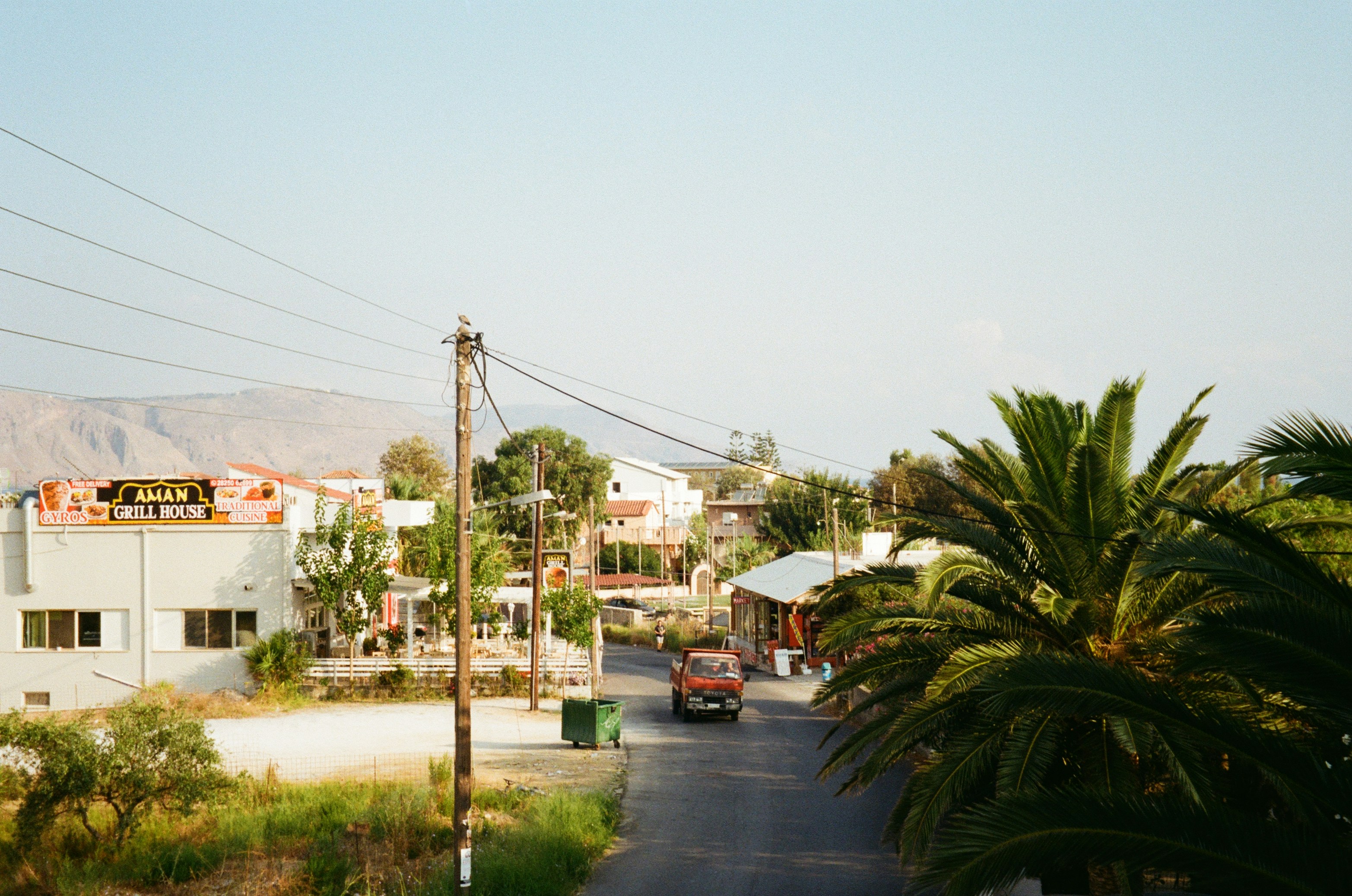 Red car on a village road with palm trees and mountains, Crete, Greece