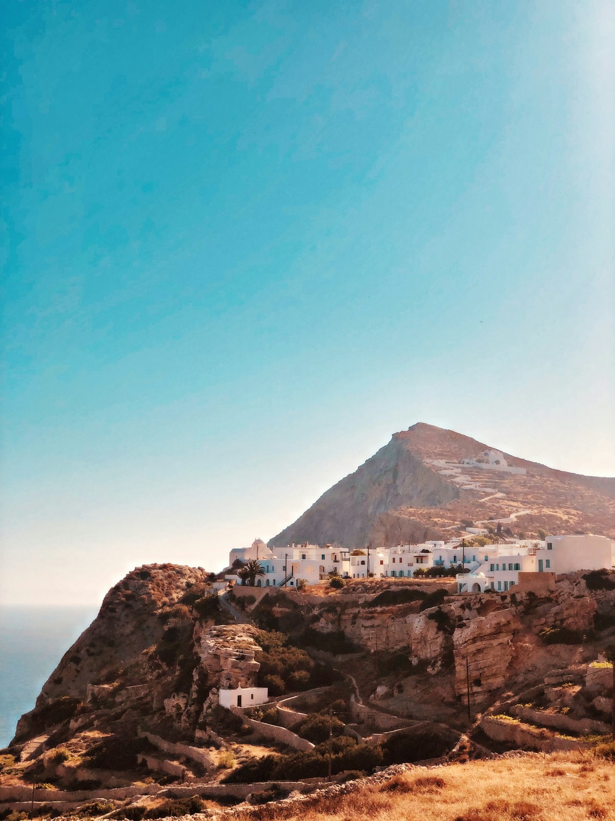 Whitewashed Chora village perched on the clifftop with a volcanic peak behind, Folegandros, Greece