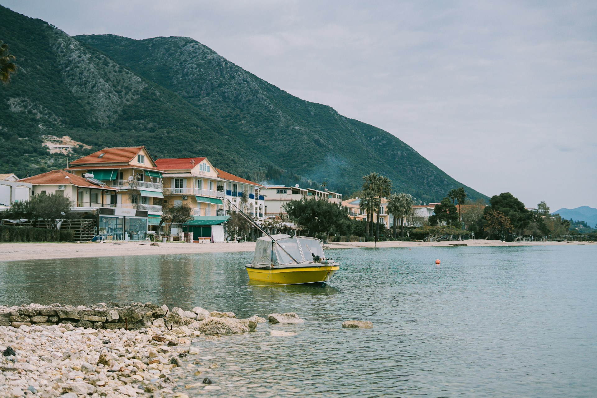 Waterfront buildings and yellow fishing boat moored in calm water at Nidri, Lefkada, Greece