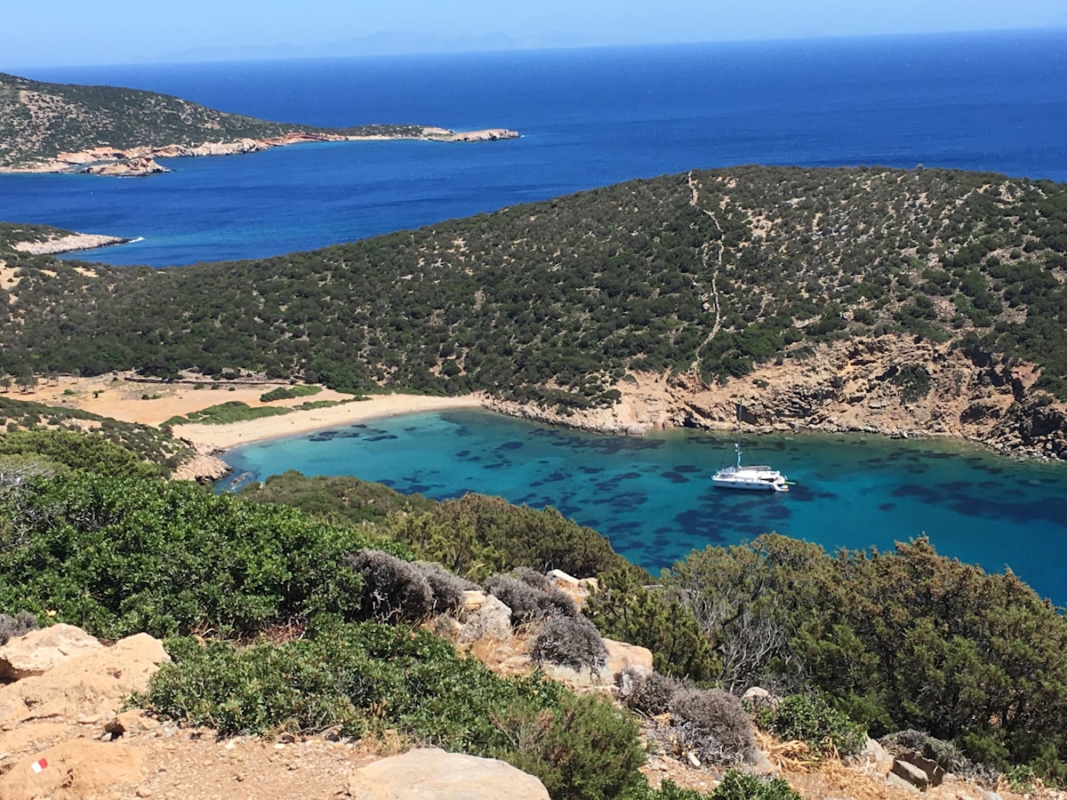 Aerial view of green hillside with hidden turquoise cove and catamaran, Sifnos, Cyclades, Greece