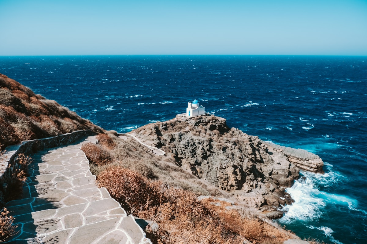 Stone path leading to the Chrissopigi chapel perched on a rocky headland above the sea, Sifnos, Greece