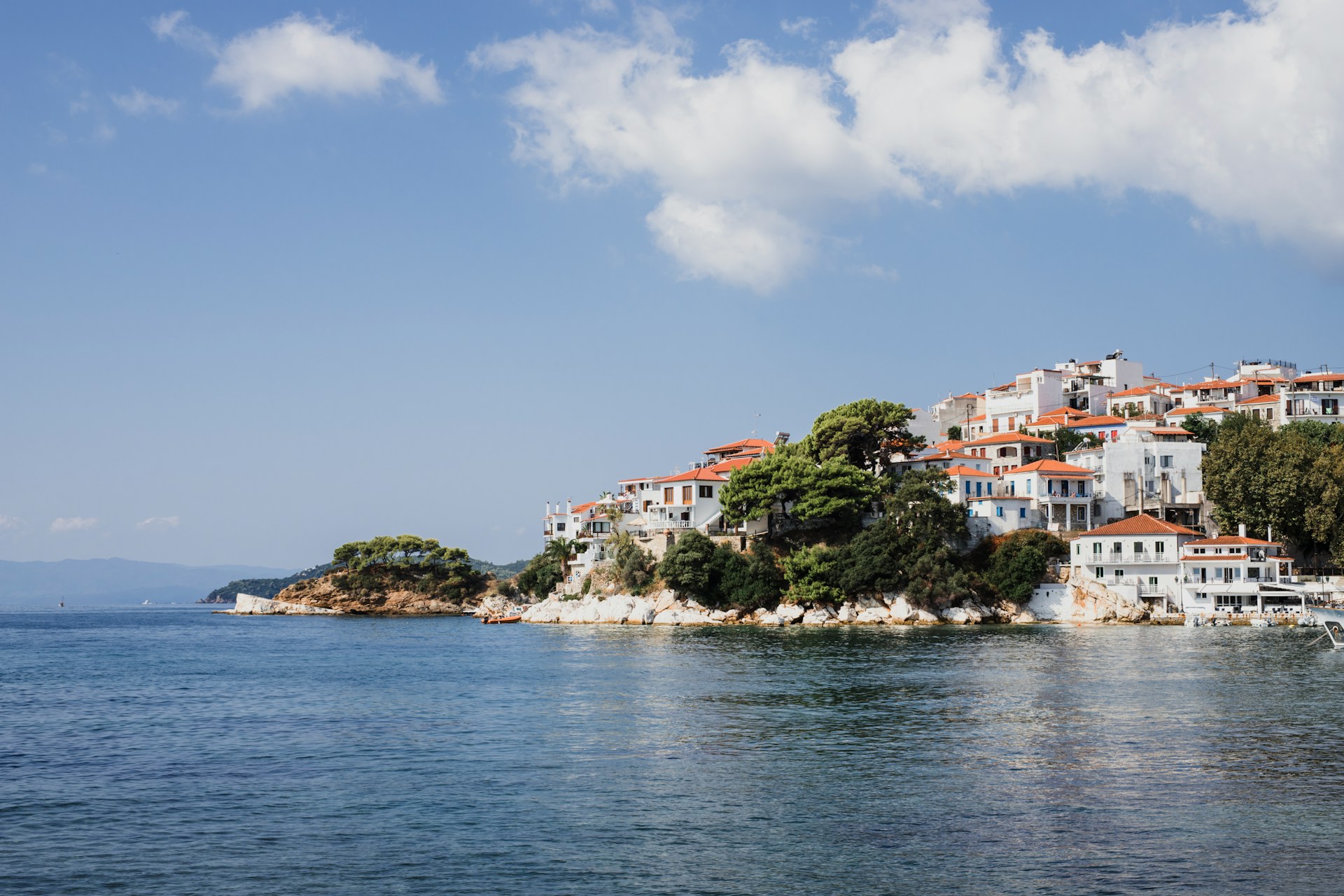 White and terracotta buildings of Skiathos Town on a rocky peninsula above blue Aegean waters, Skiathos, Greece