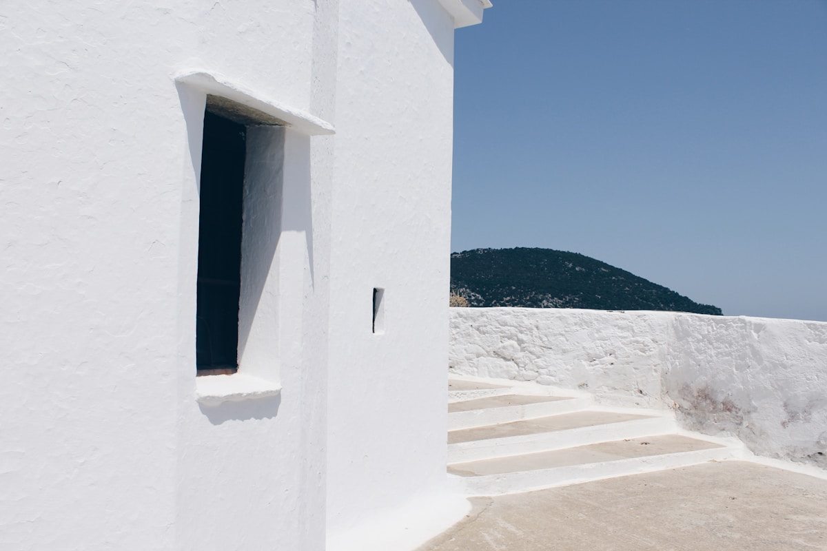 White chapel with stone steps and view of forested green hill, Skopelos, Sporades, Greece