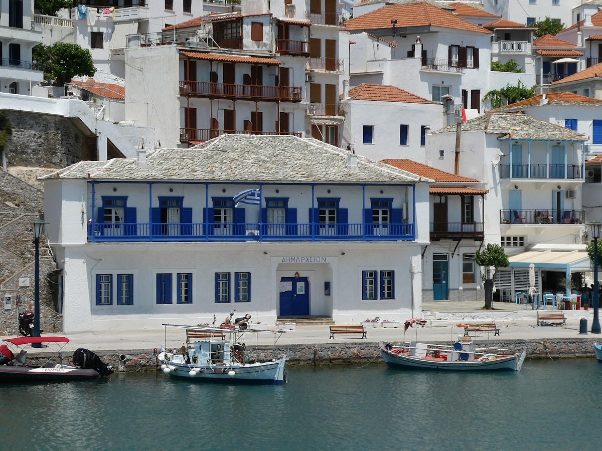 Traditional blue-shuttered building at Skopelos Town harbour with fishing boats and hillside town behind, Greece