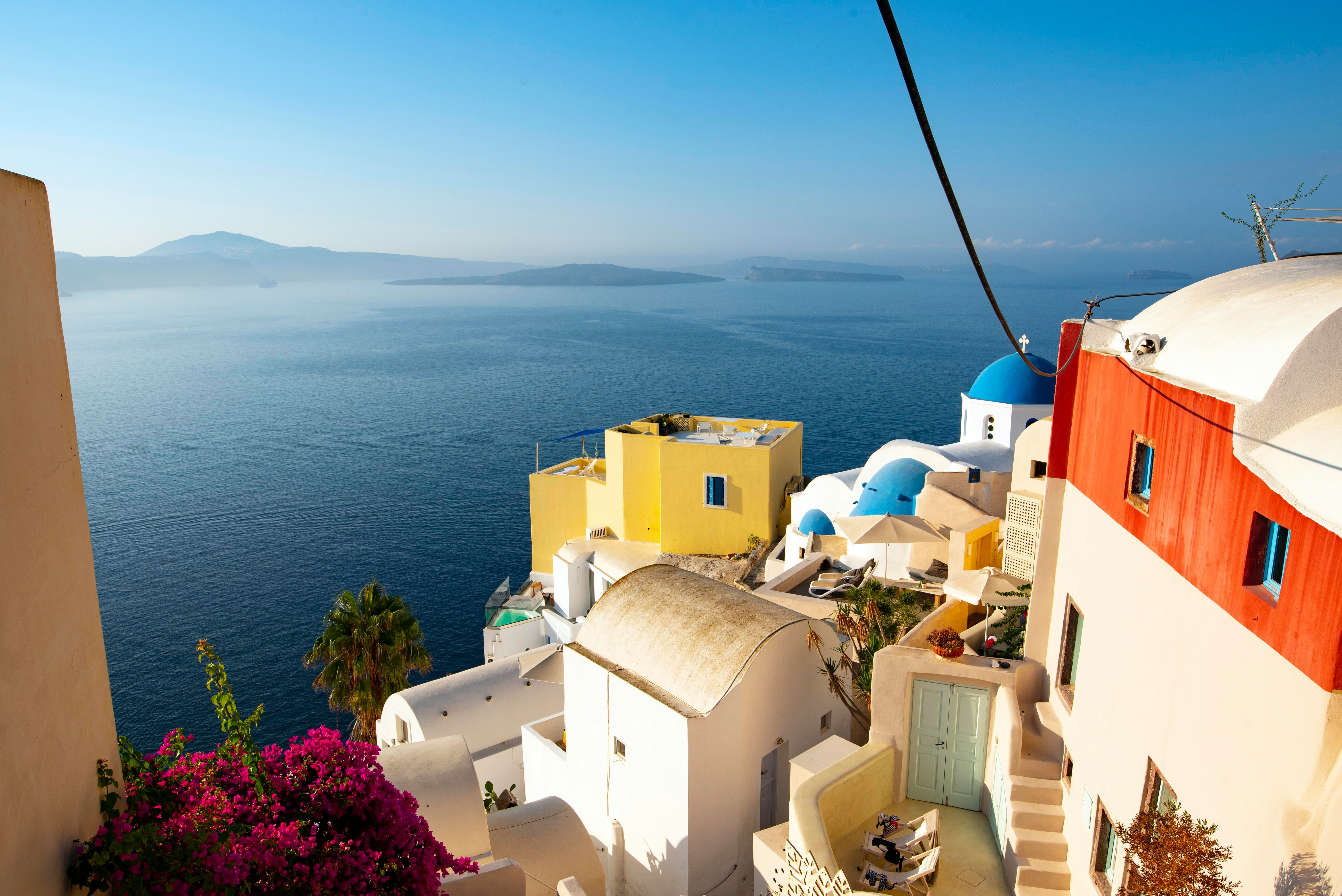 Colourful white and yellow buildings cascading down a hillside with blue domes and bougainvillea, Dodecanese, Greece
