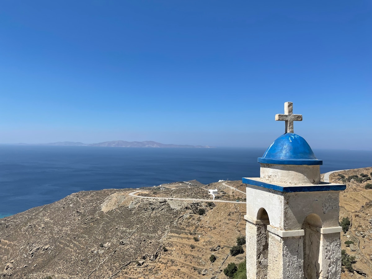 Blue-domed chapel tower with stone cross overlooking the Aegean Sea and distant islands, Tinos, Greece