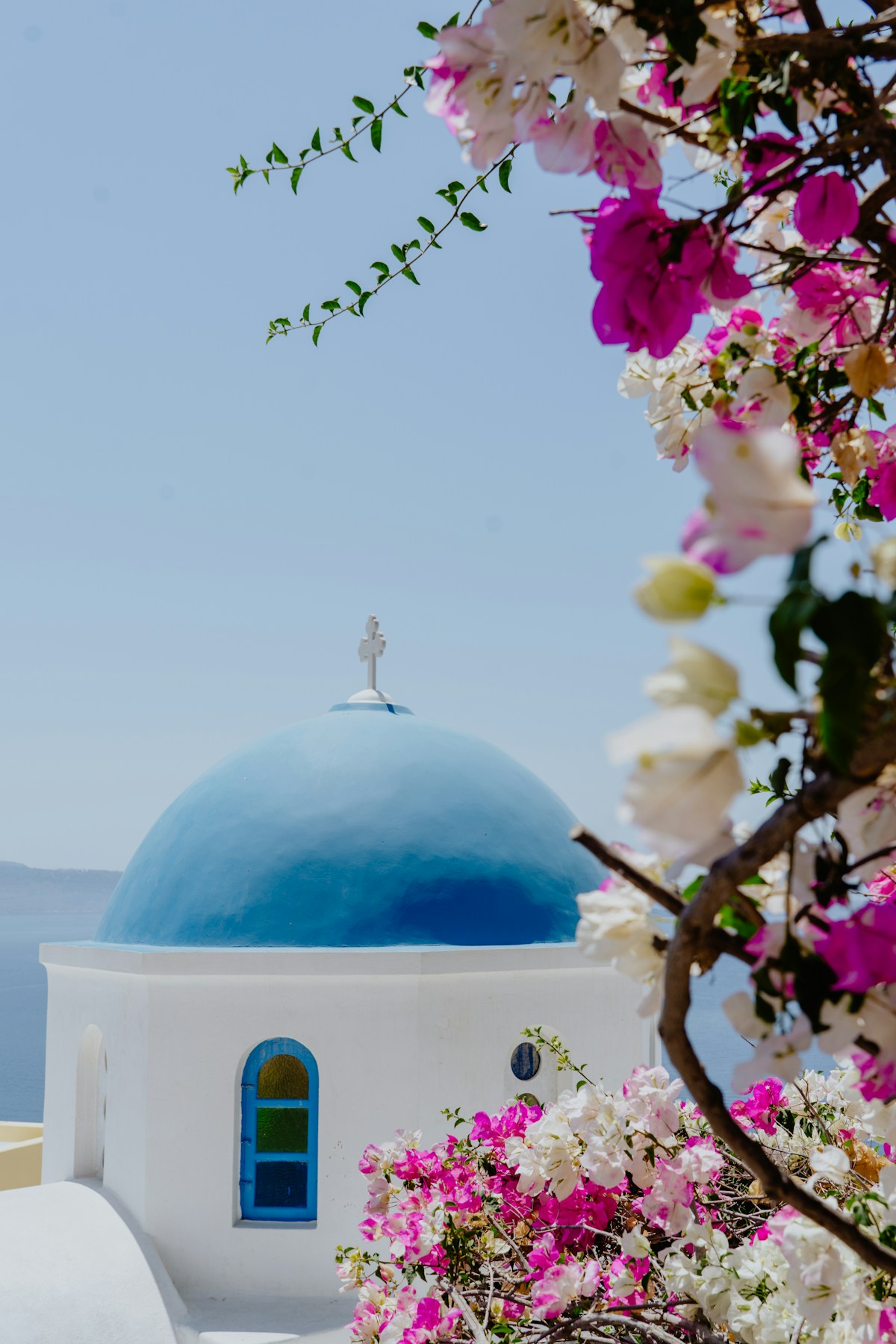 Blue dome chapel framed by bougainvillea flowers in Oia, Santorini