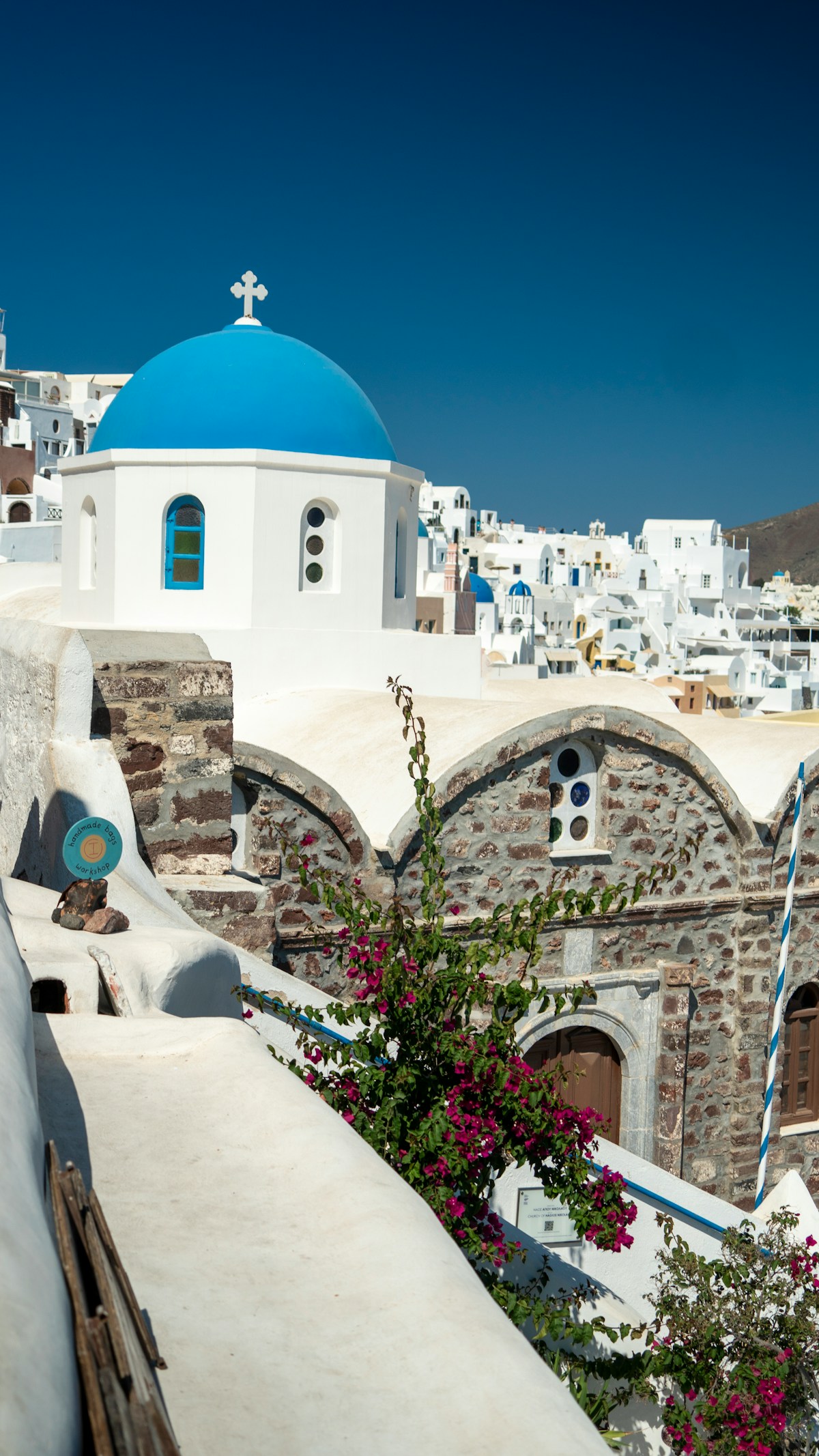 White chapel with blue dome and pink bougainvillea in a Cycladic village, Santorini Greece