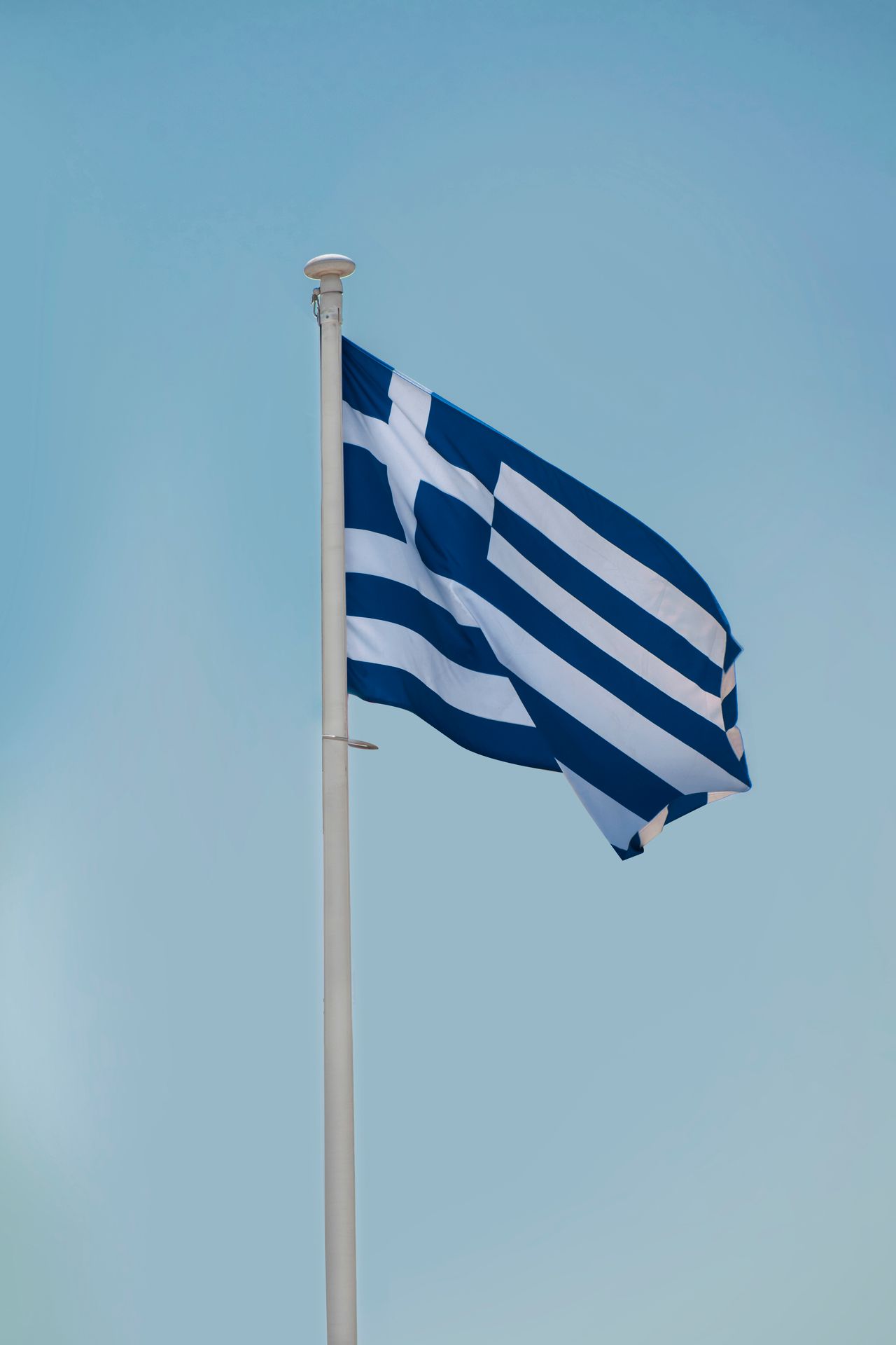 Greek national flag waving on a flagpole against a blue sky