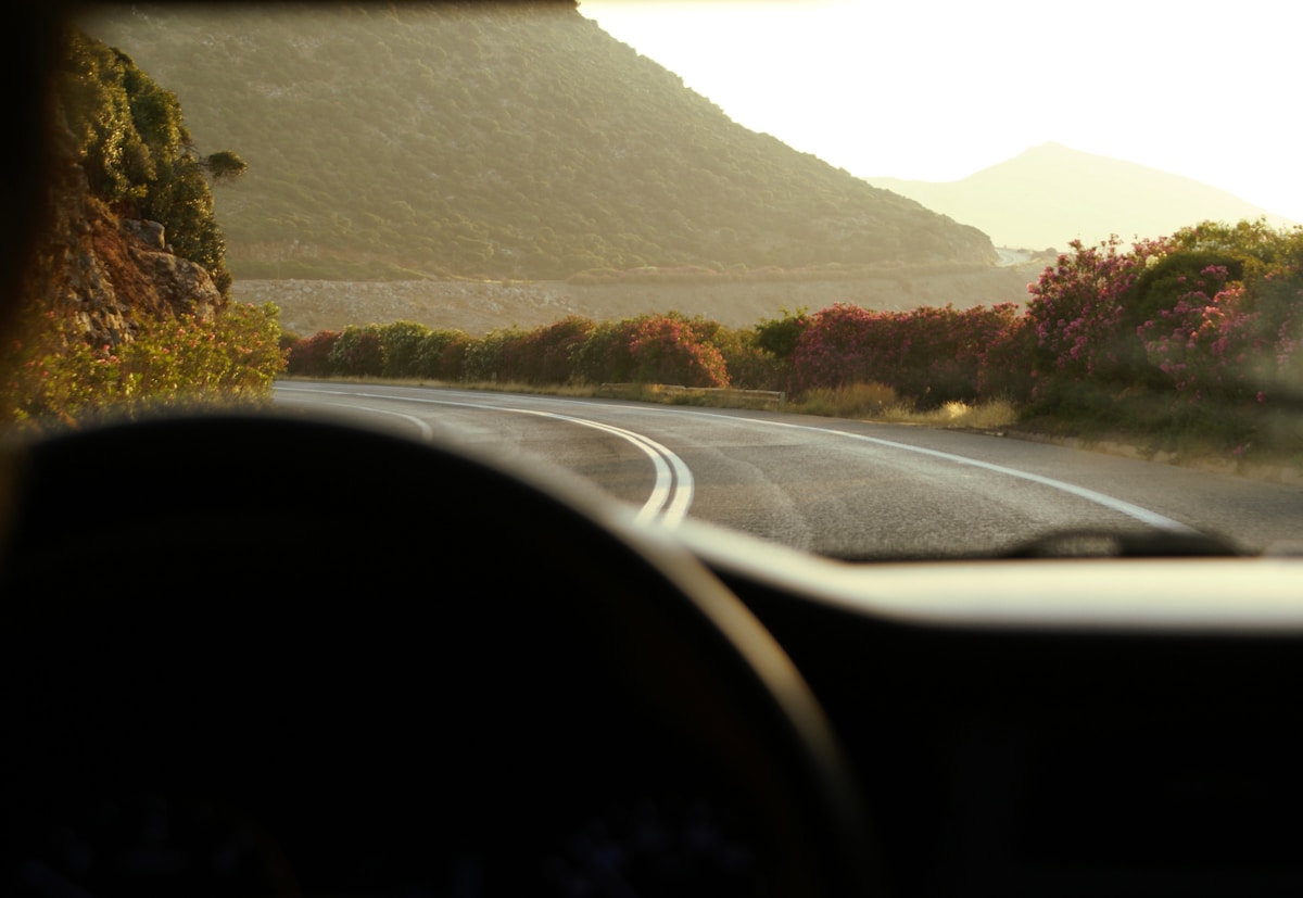 View from inside a car on a winding road through rocky hills and bougainvillea, Crete Greece
