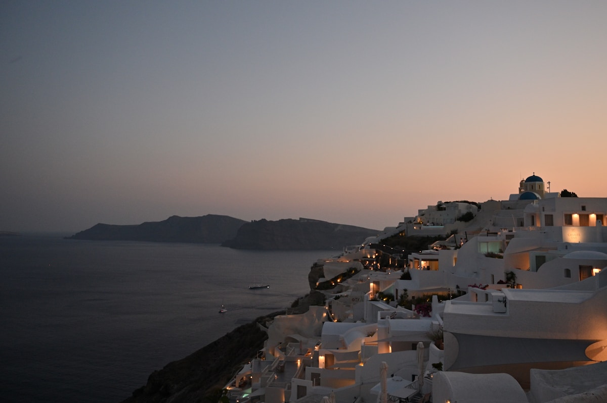 White Santorini cliff-top buildings and blue-domed church glowing at dusk above the caldera