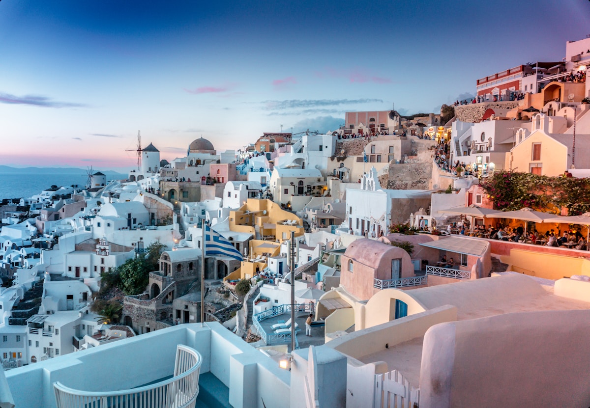 Oia village at sunset with Greek flag and whitewashed buildings, Santorini, Greece