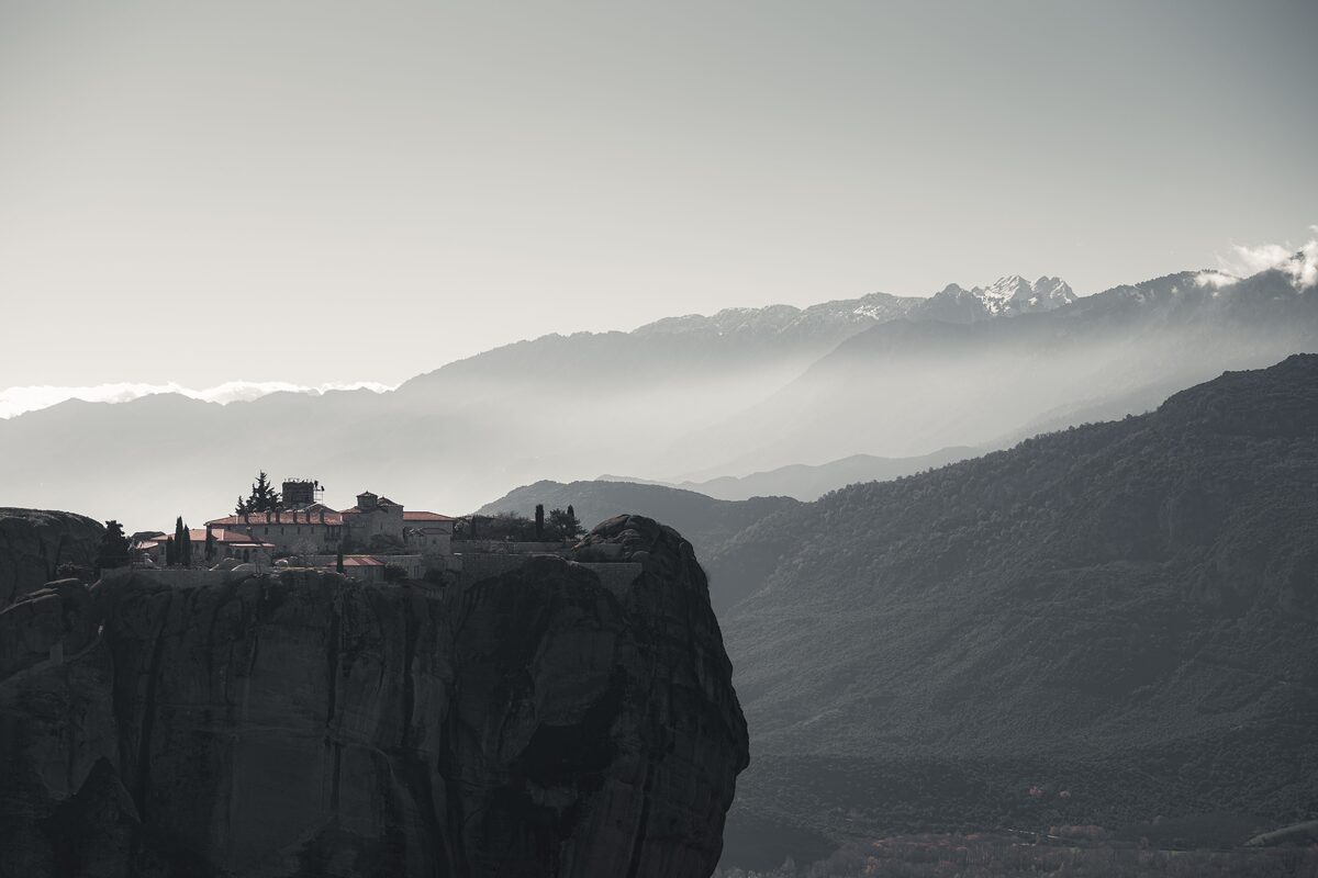 Orthodox monastery perched on Meteora rock with snow-capped mountains and mist in the valley, Greece