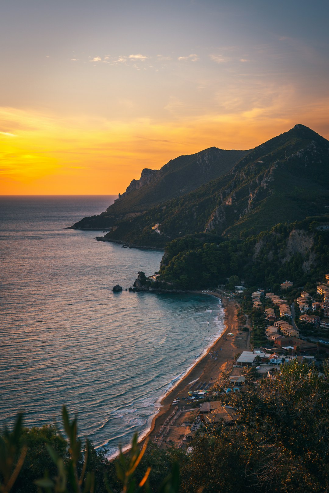 Aerial view of a sandy Corfu beach curving along a turquoise bay at golden sunset