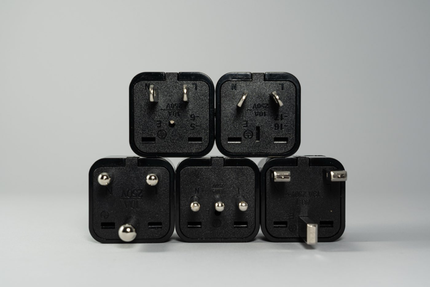 Stack of five black travel plug adapters with different pin layouts on a grey background