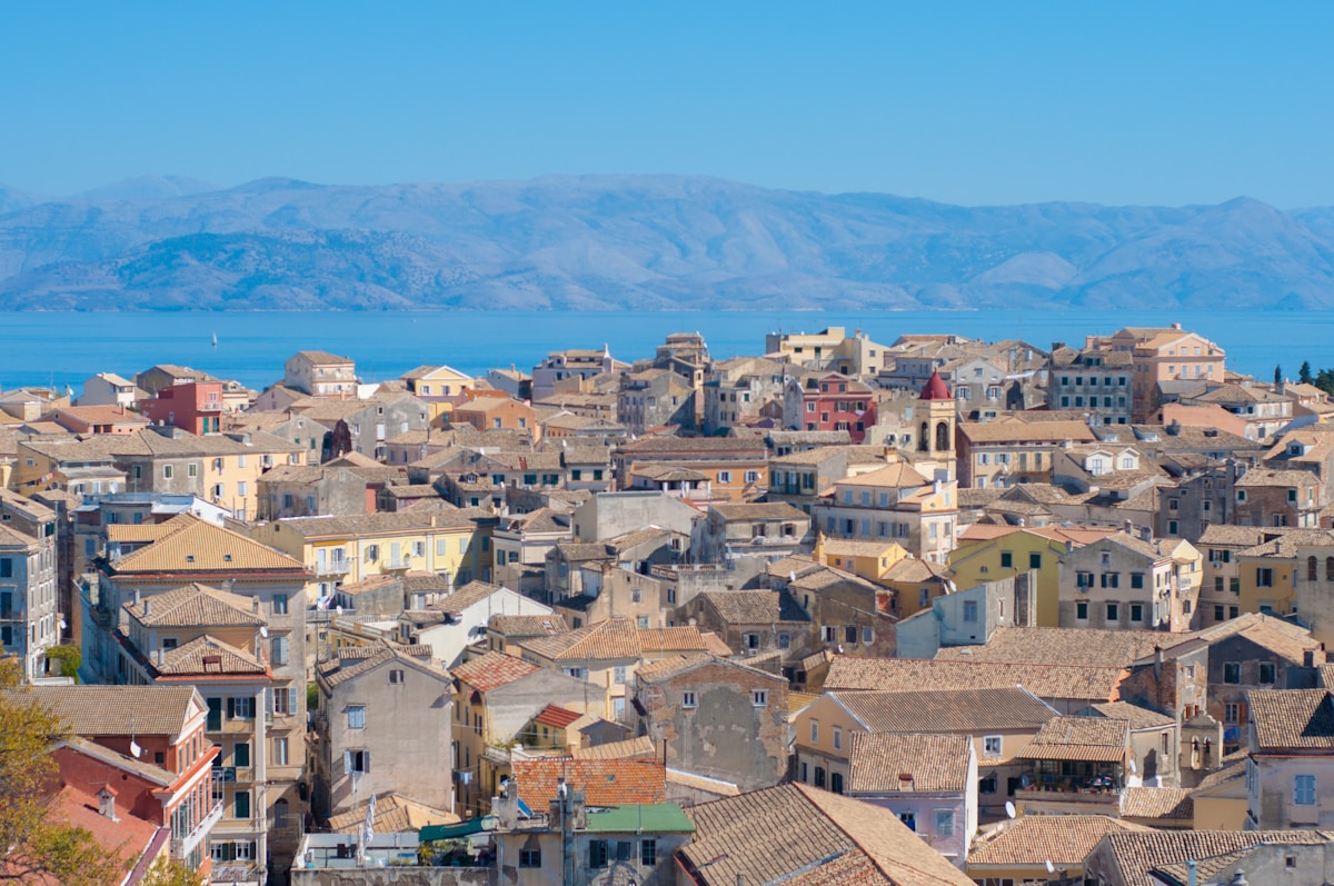 Aerial view of Corfu Town's terracotta rooftops and Venetian architecture with mountains and sea behind
