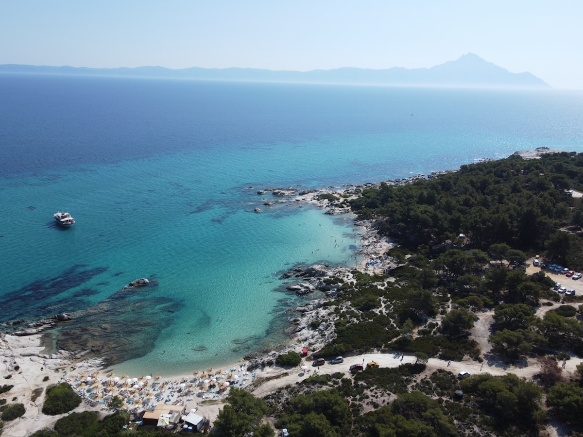 Aerial view of turquoise water and pine-covered beaches at Halkidiki, with the Mount Athos peninsula visible in the distance