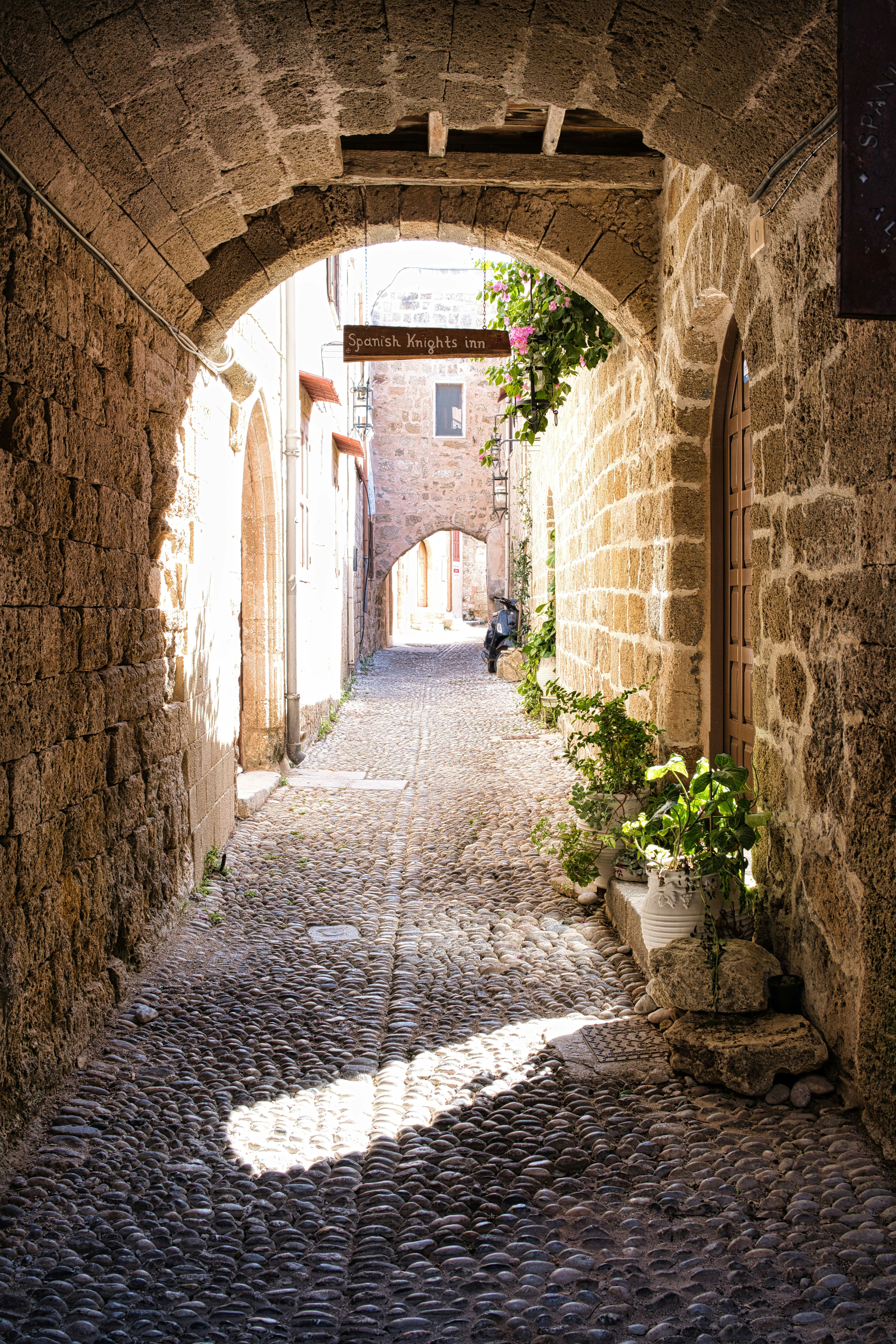 Cobblestone alleyway with stone archway and sunlight, Rhodes Old Town, Greece