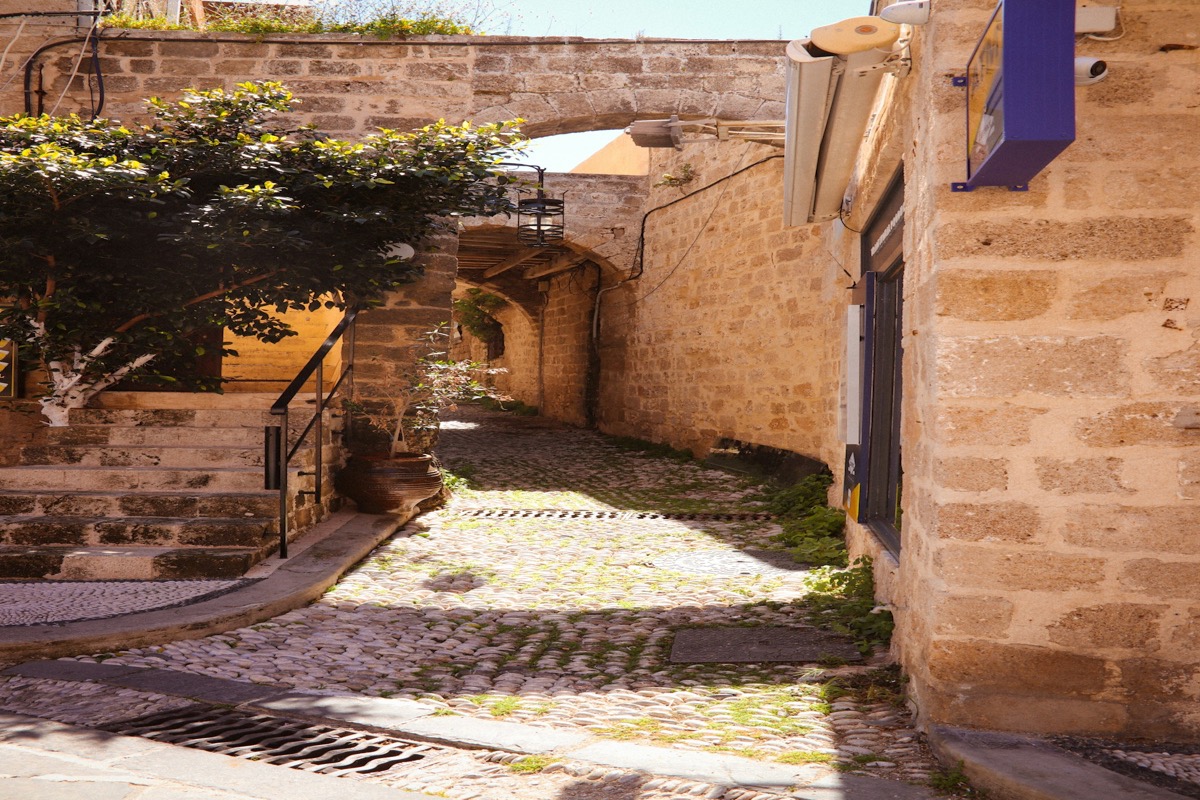 A sunlit cobblestone lane with stone archways in Rhodes Old Town, Greece