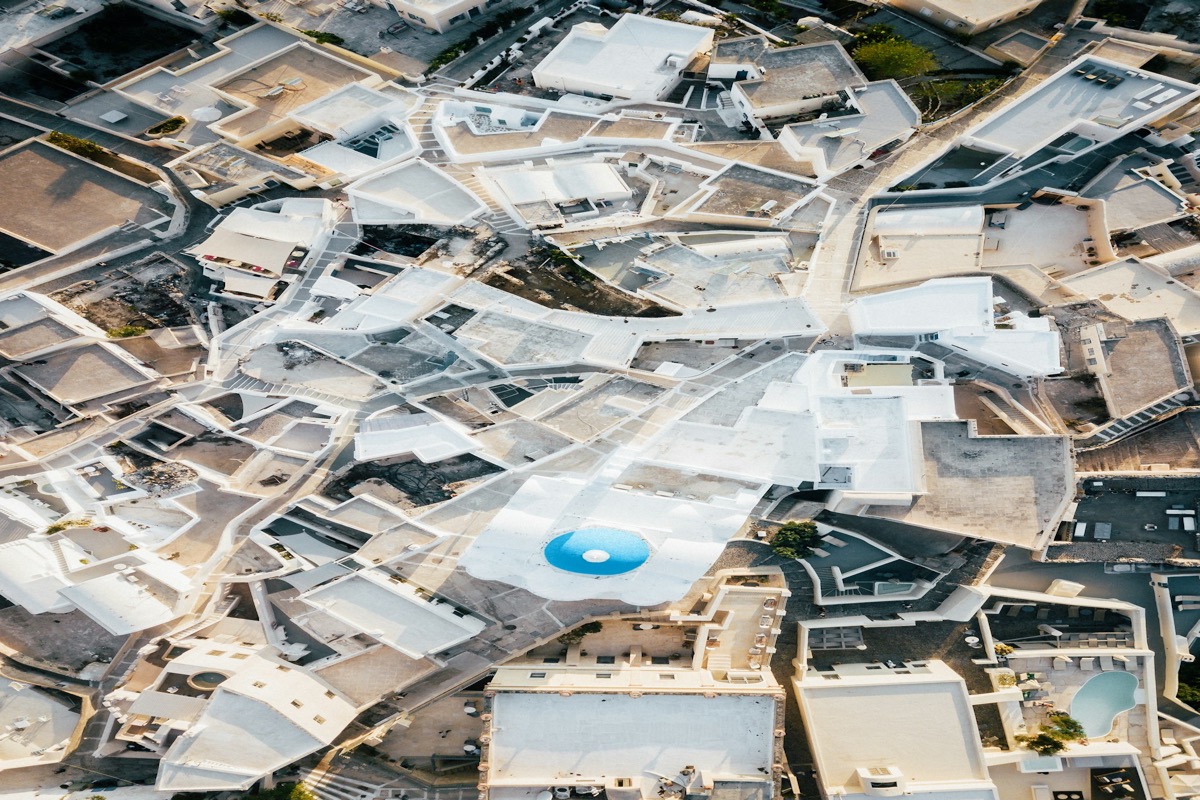 Aerial view of Santorini's whitewashed rooftops with a blue pool visible from above